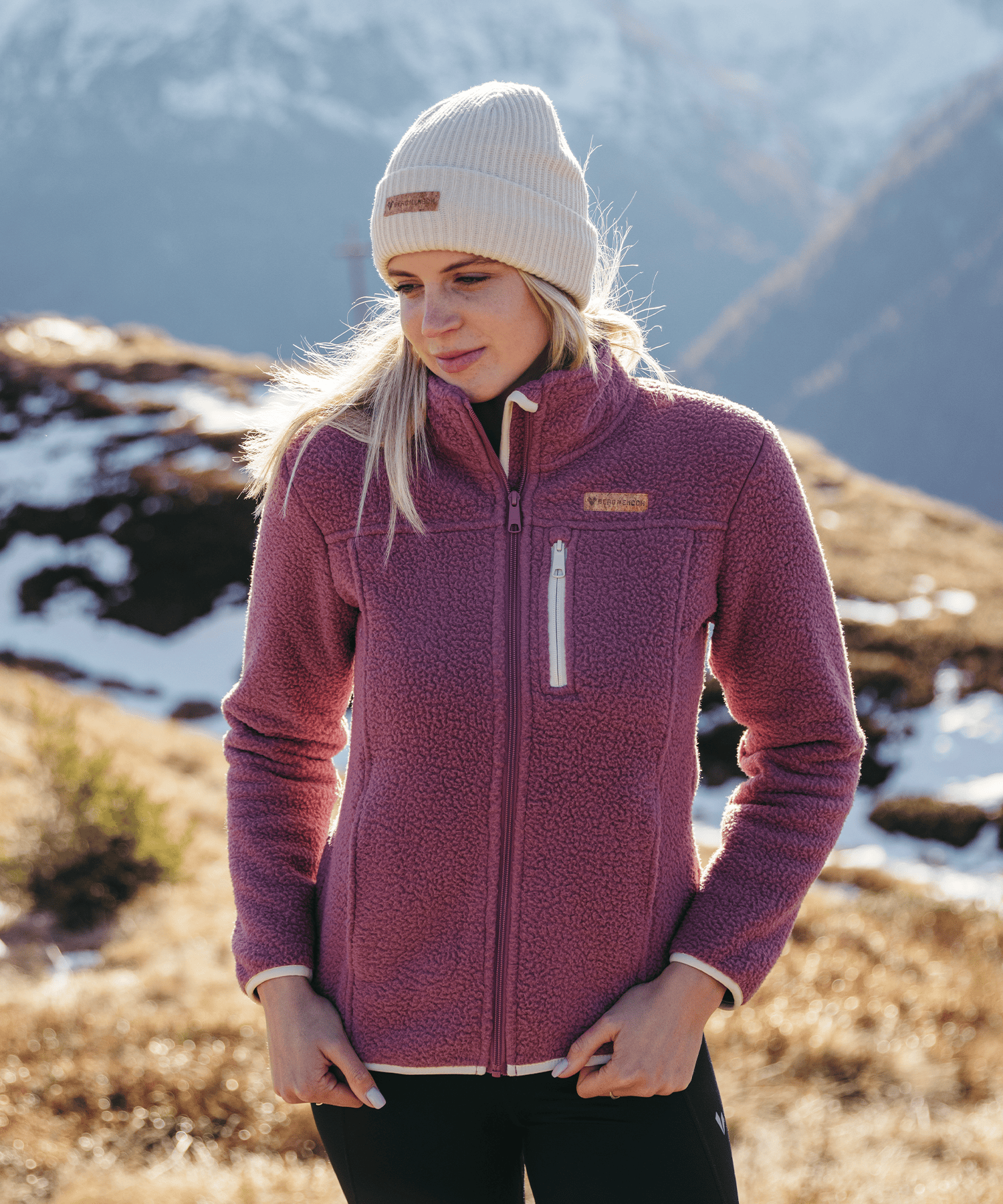 Model trägt die BERGMENSCH Damen Sherpa Fleece Jacke in der Farbe Hibiscus und die Cozy Fleece Beanie in der Farbe Whitecap Grey