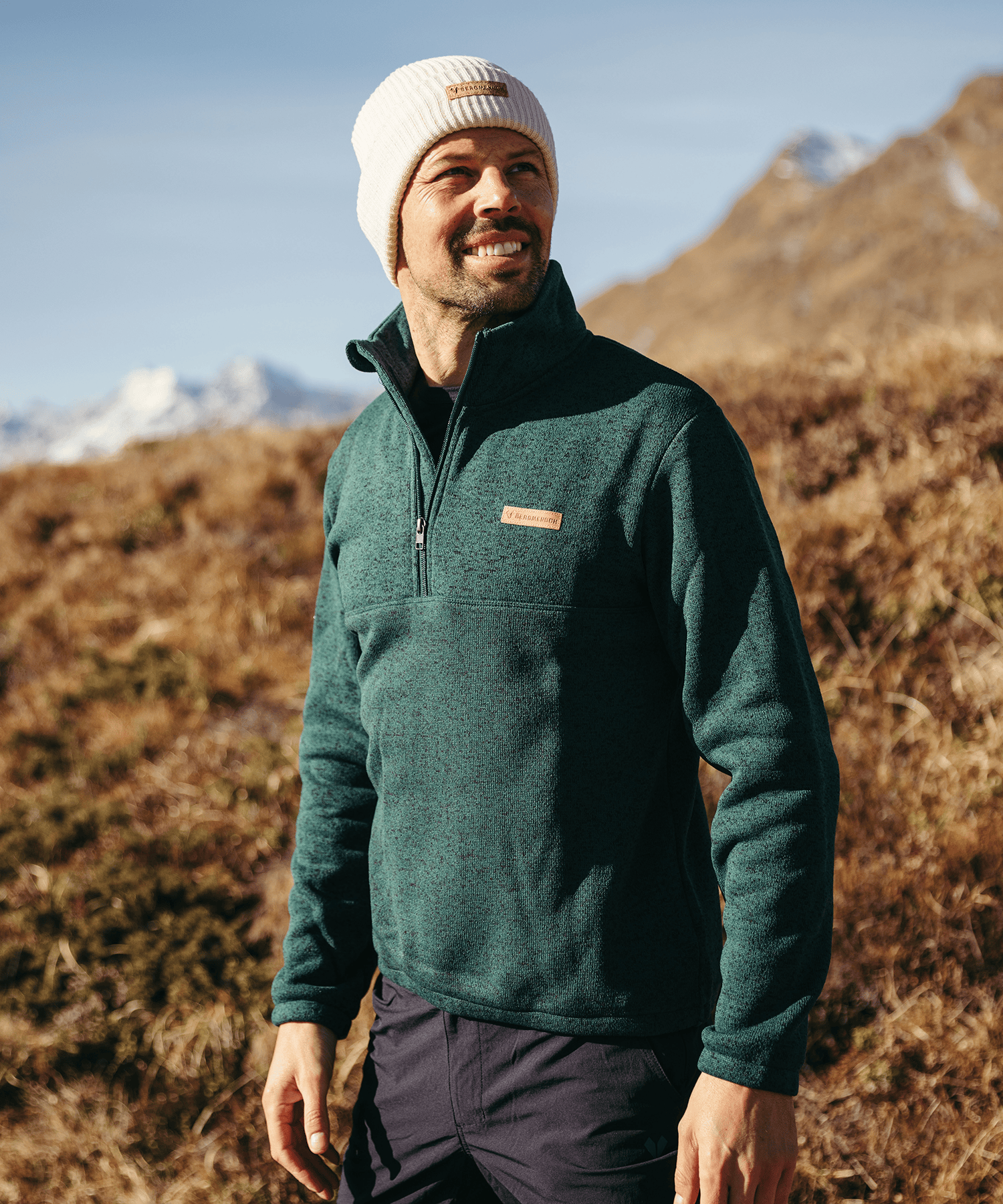 Model trägt den BERGMENSCH Herren Half-zip Strickfleece in Piniengrün in den Bergen