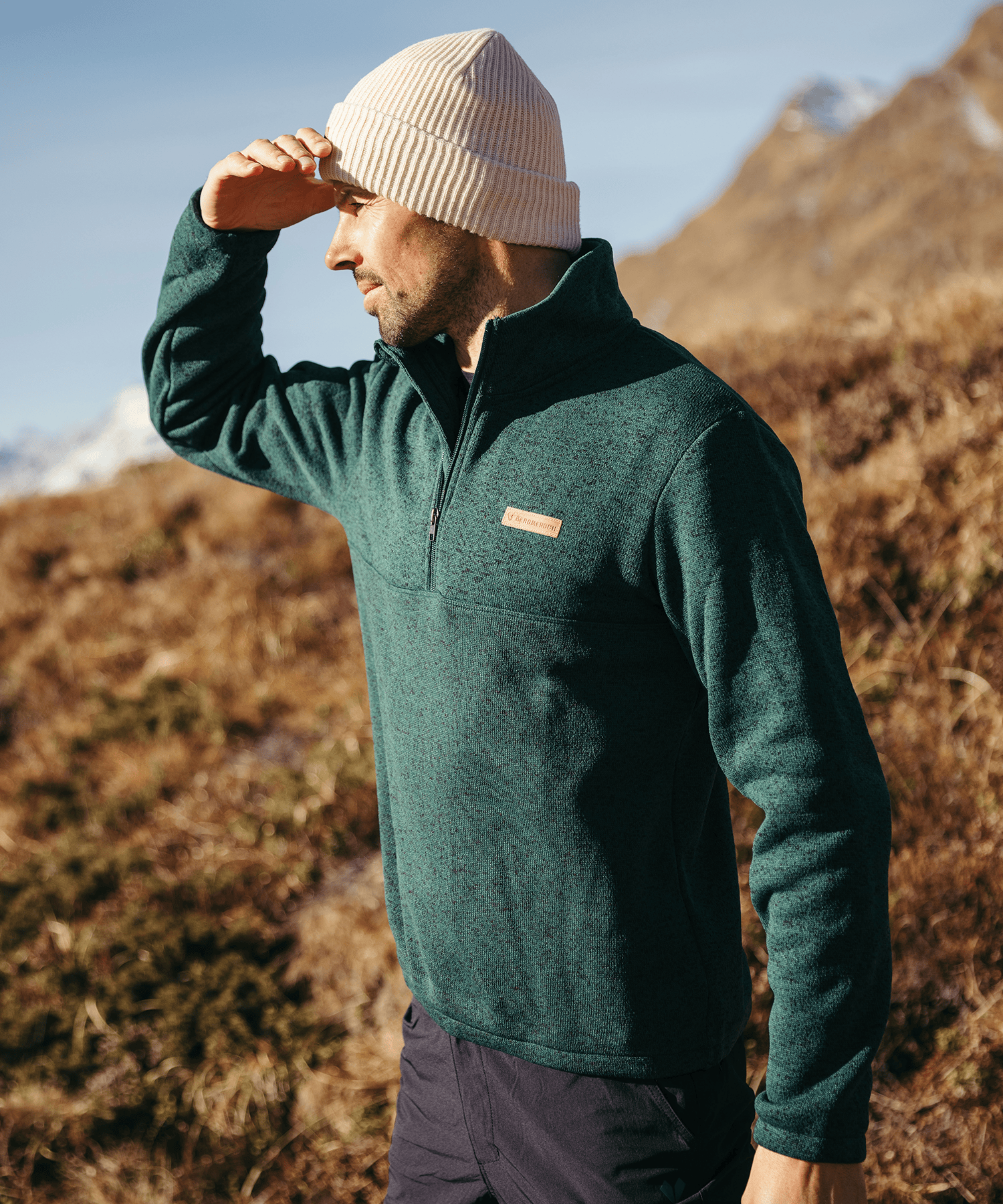 Model trägt den BERGMENSCH Herren Half-zip Strickfleece in Piniengrün in den Bergen