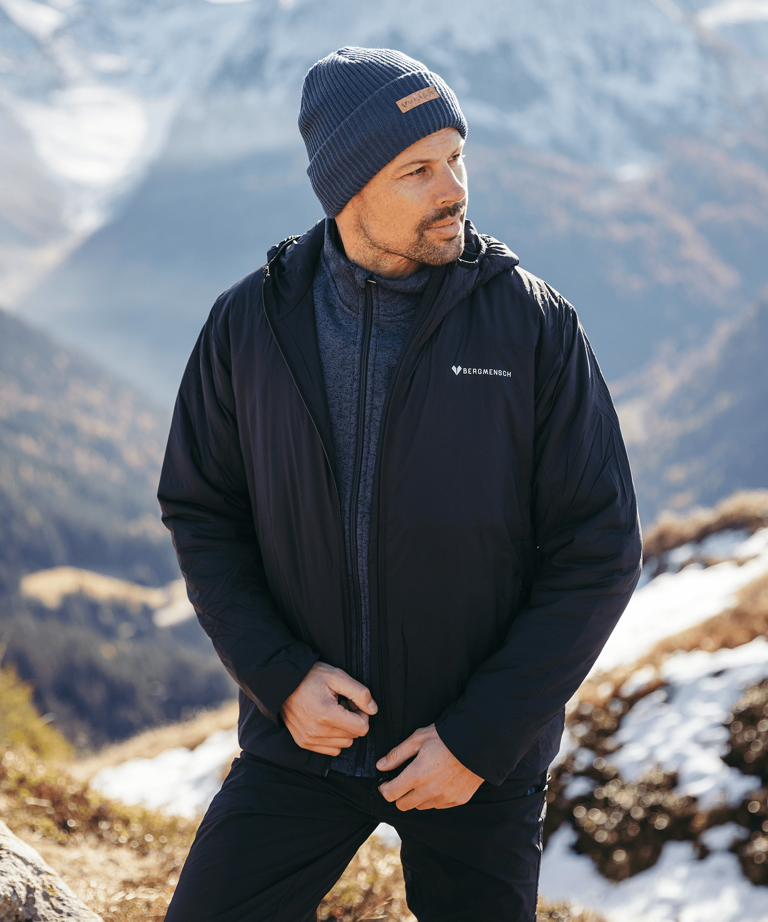 Model trägt die BERGMENSCH Herren Thermolite Jacke in Schwarz und die Cozy Fleece Beanie in Midnight Navy