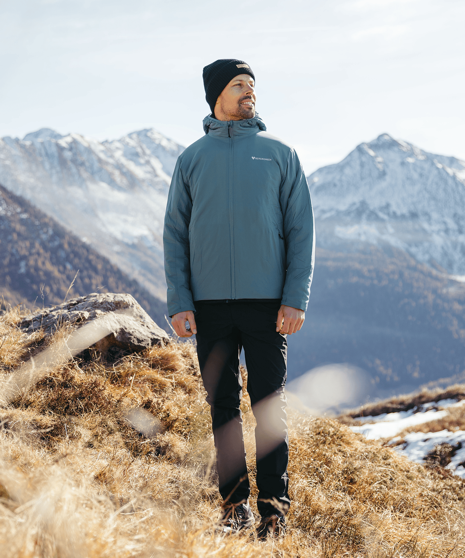 Model trägt die BERGMENSCH Herren Thermolite Jacke in Deep Lake und die Cozy Fleece Beanie in Midnight Navy