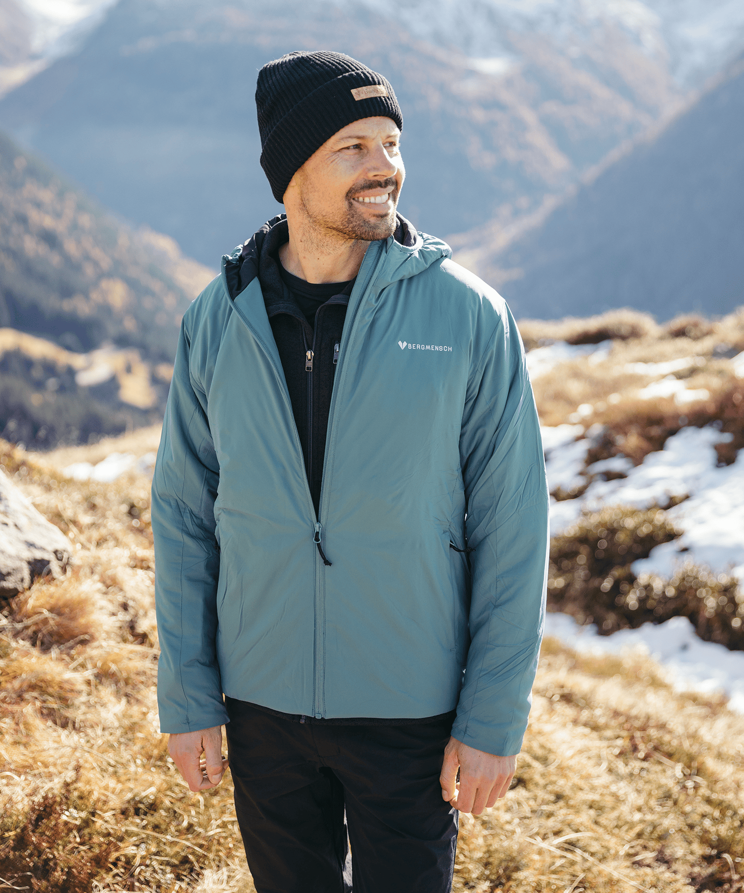 Model trägt die BERGMENSCH Herren Thermolite Jacke in Deep Lake und die Cozy Fleece Beanie in Midnight Navy